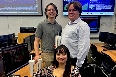 A trio of business students hold Bloomberg tumblers in the SMART Lab. They wear professional attire.