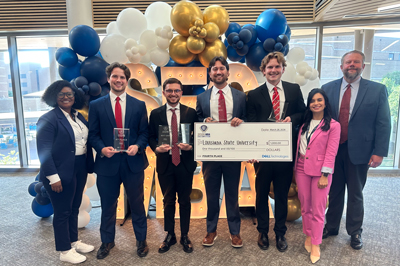 Flores MBA team holds a large cardboard check in front of a balloon display.